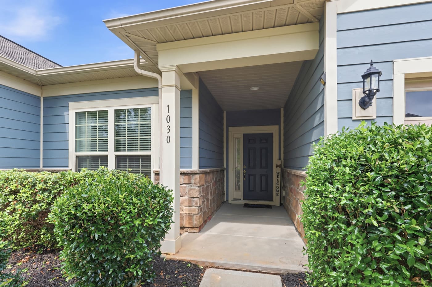 The covered front porch, with the house number 1030 on the column and stone veneer below the siding.