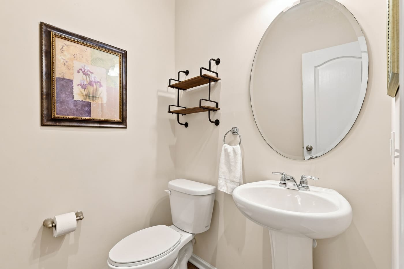 The powder room with a pedestal sink and oval mirror.